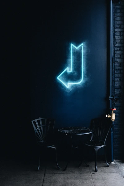 Neon Arrow Sign on Dark Wall with Chairs and Table