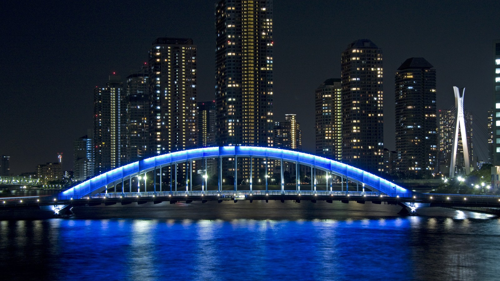 Vista elevada de uma ponte sobre um rio com uma cidade ao fundo (ponte, noite, cidade, metrópole, marco)