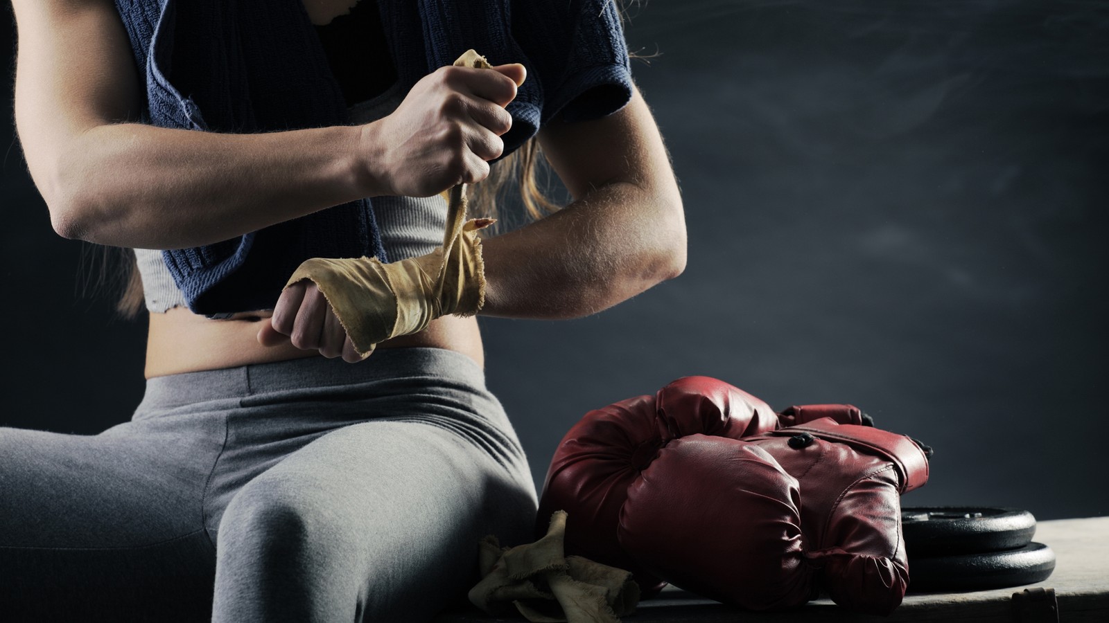 Una mujer con una camisa azul y pantalones grises con guantes de box (boxeo, guante de boxeo, boxeo femenino, kickboxing, entrenamiento de boxeo)