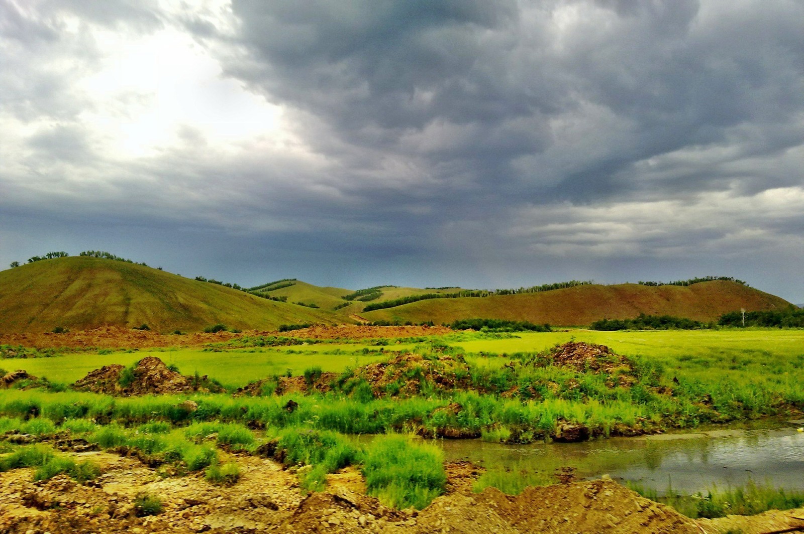 Vista de um campo com um rio e colinas ao fundo (pradaria, terras altas, colina, pastagem, céu)