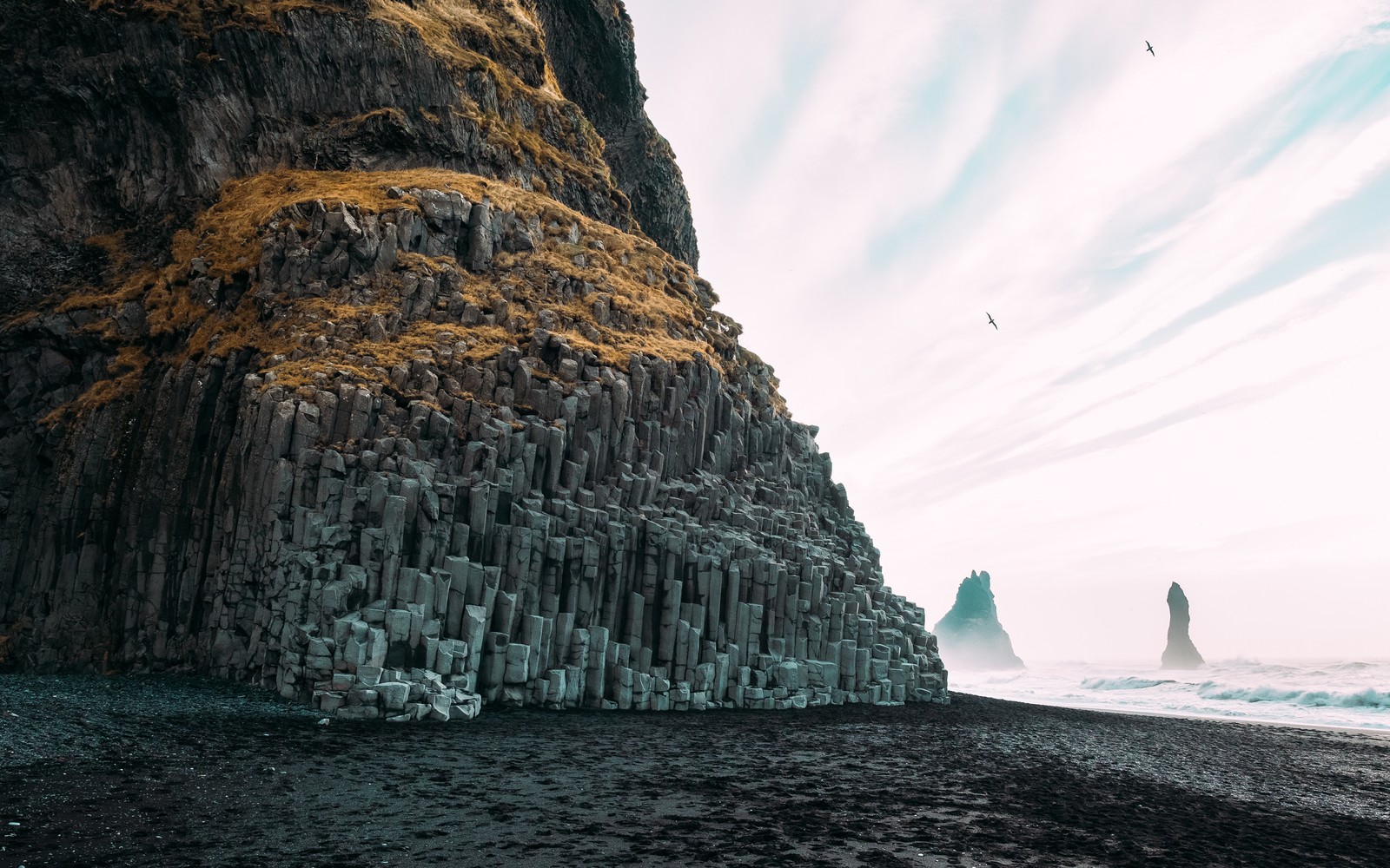 Un primer plano de una playa de arena negra con una formación rocosa (playa, naturaleza, arena, mar, nube)