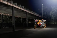 Repsol Honda CBR1000RR-Motorrad, das nachts beleuchtet ist, unter einer schwach beleuchteten Struktur geparkt.