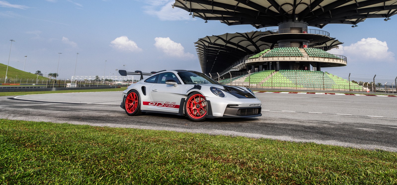 Um close de um carro branco em uma pista perto de um edifício (porsche 911 gt3 rs, pacote weissach, 2023, 5k, 8k)