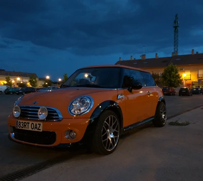 Mini Cooper R56 naranja estacionado al anochecer con un fondo de cielo dramático.