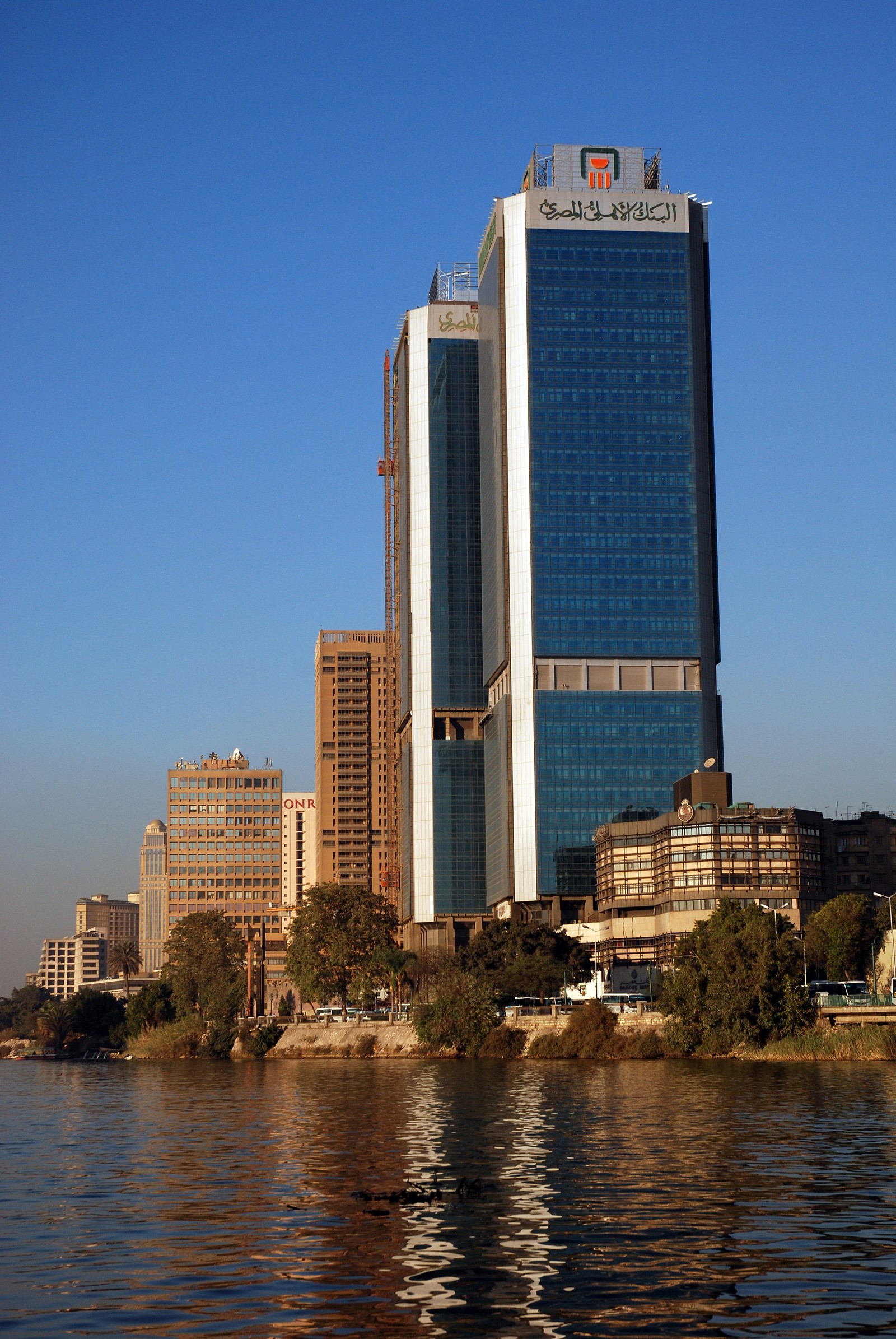 Buildings on the shore of a river with a boat in the water (cairo, skyscraper, skyline, daytime, landmark)