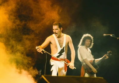 Freddie Mercury captivates the audience with a powerful performance, while Brian May accompanies on guitar, set against a vibrant, smoke-filled stage.