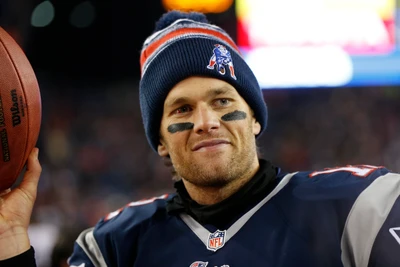 Tom Brady in New England Patriots Ausrüstung, lächelnd mit einem Football in der Hand