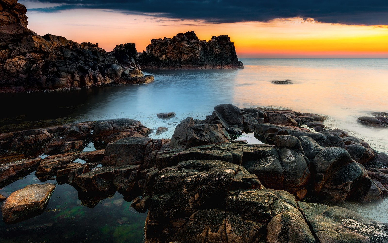 Vue d'une plage rocheuse avec un coucher de soleil en arrière-plan (côte rocheuse, orange coucher de soleil, formations rocheuses, paysage marin, océan)