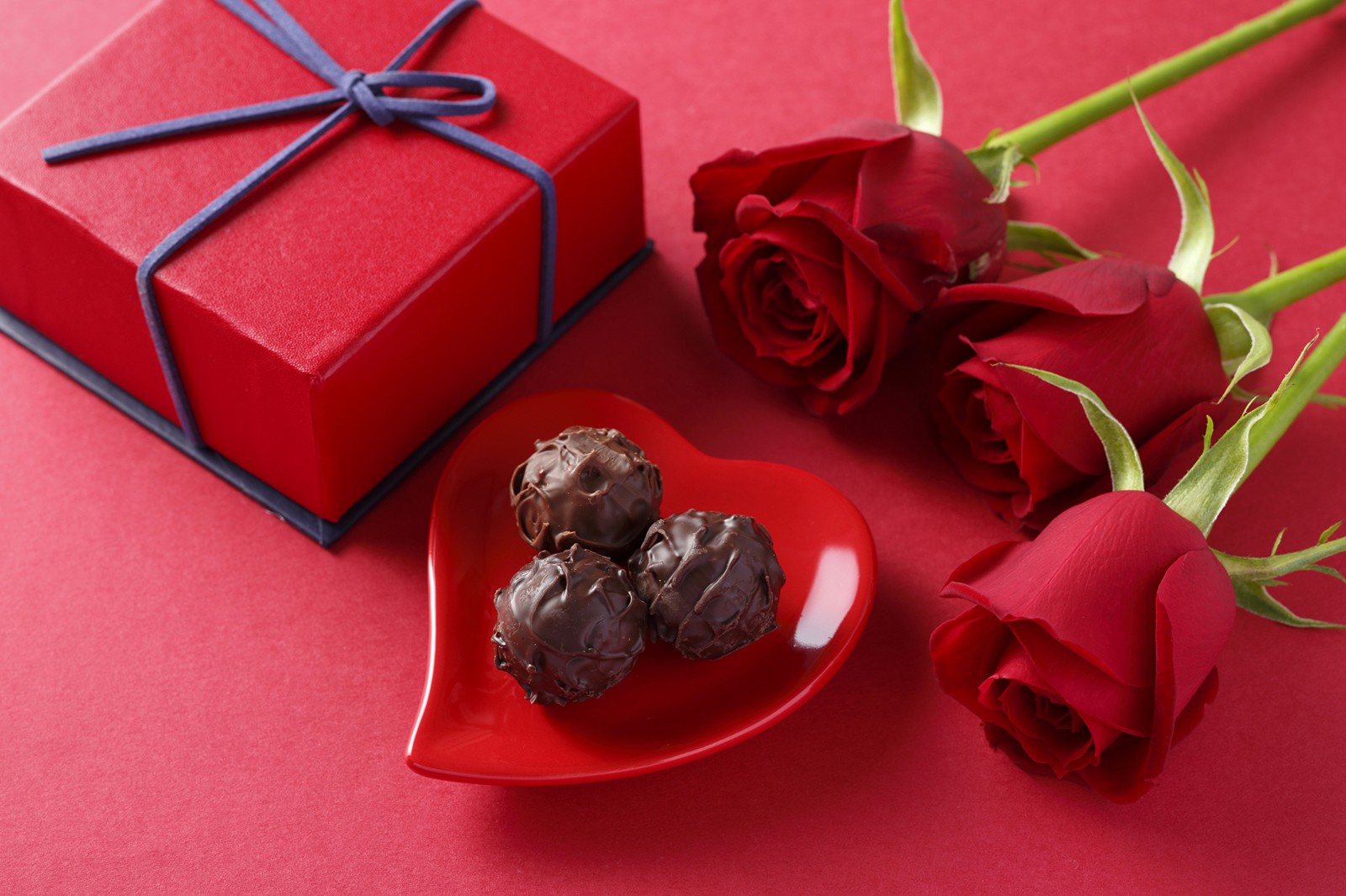 Rosas y chocolates en un tazón con forma de corazón rojo junto a una caja roja (chocolate, dulces, día de san valentín, praliné, confitería)