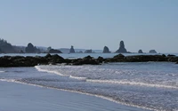 Ondas suaves batendo contra uma costa rochosa sob um céu claro, com silhuetas de formações costeiras ao longe.