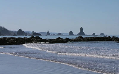 Suaves olas golpeando contra una costa rocosa bajo un cielo despejado, con siluetas de formaciones costeras a lo lejos.