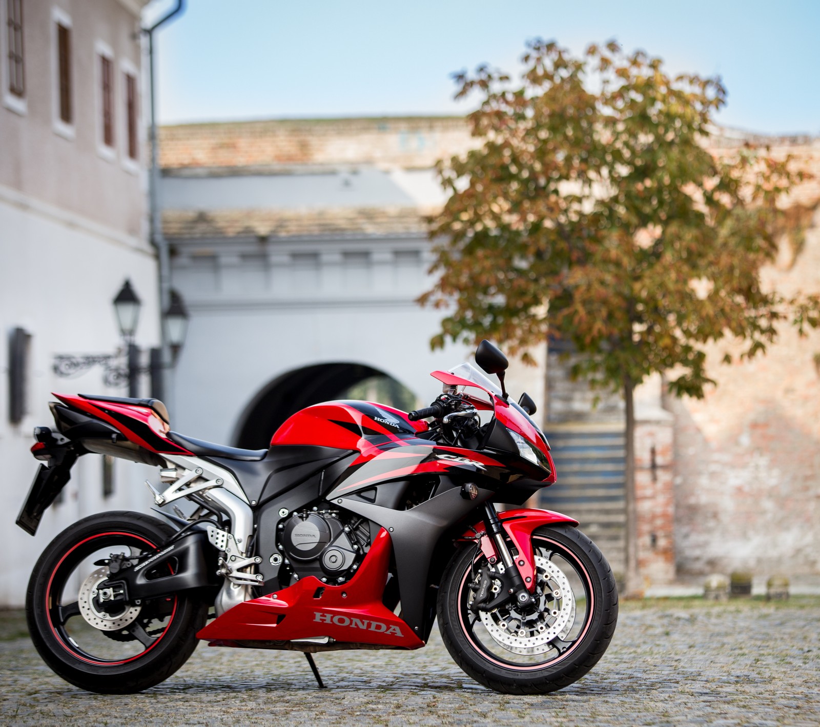 Moto rouge arabe garée sur des pavés devant un bâtiment (cbr 600 rr, honda)