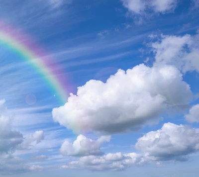 Lebendige Regenbogen, der durch einen blauen Himmel mit flauschigen weißen Wolken spannt