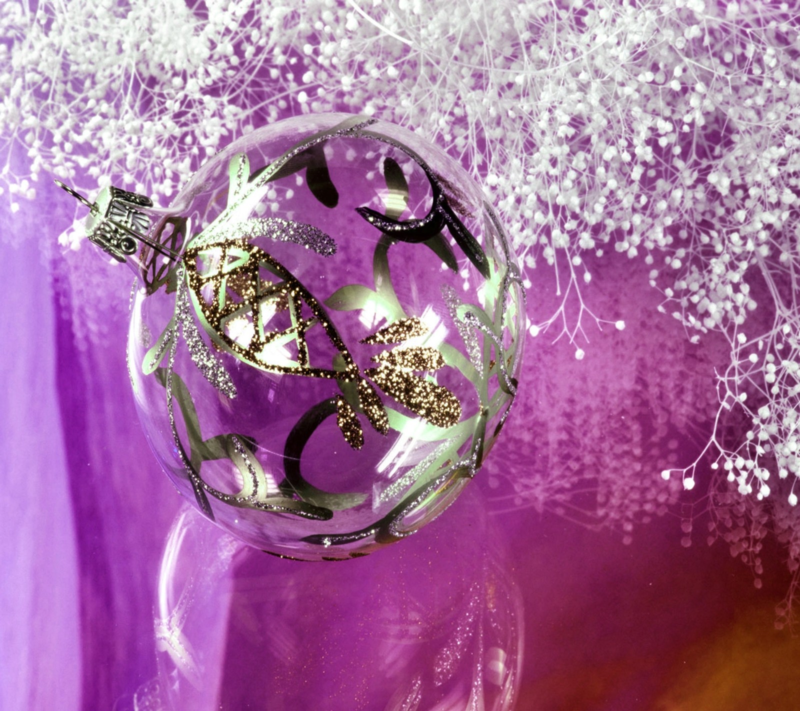 There is a glass ball with a gold decoration on it (ball, christmas, silver, white, xmas)