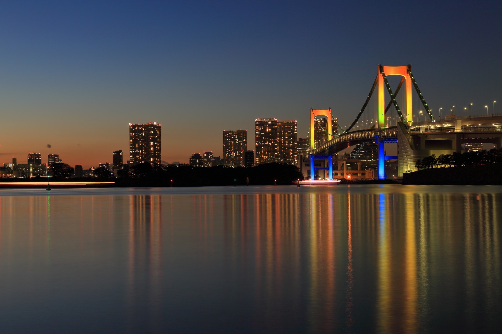 Uma vista de uma ponte sobre um corpo d'água com uma cidade ao fundo (ponte arco íris, paisagem urbana, reflexo, linha do horizonte, cidade)