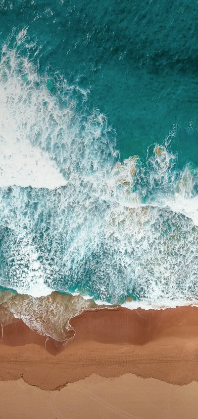 Aerial view of turquoise ocean waves gently meeting a sandy beach.