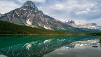 Majestosa cadeia de montanhas refletindo em um tranquilo lago glacial, cercada por exuberantes florestas de montanha.