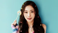 Youngeun from Kep1er holding a colorful lollipop, styled with vibrant hair accessories against a bright blue background.