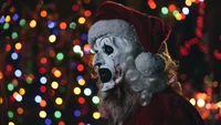 Art le clown en costume de Père Noël au milieu des lumières de fête colorées