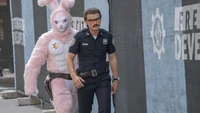 Un policier marche avec confiance dans la rue, suivi de près par une personne dans un grand costume de lapin rose, soulignant un moment comique et surréaliste du film "Free Guy".