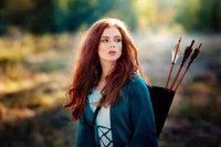 A beautiful woman with long, flowing red hair stands in a natural setting, wearing a blue outfit and carrying a quiver of arrows, exuding a sense of strength and elegance.