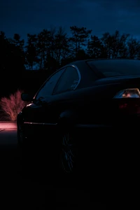 Voiture de sport noire élégante illuminée contre un fond crépusculaire, mettant en valeur ses lignes élégantes et son design automobile.