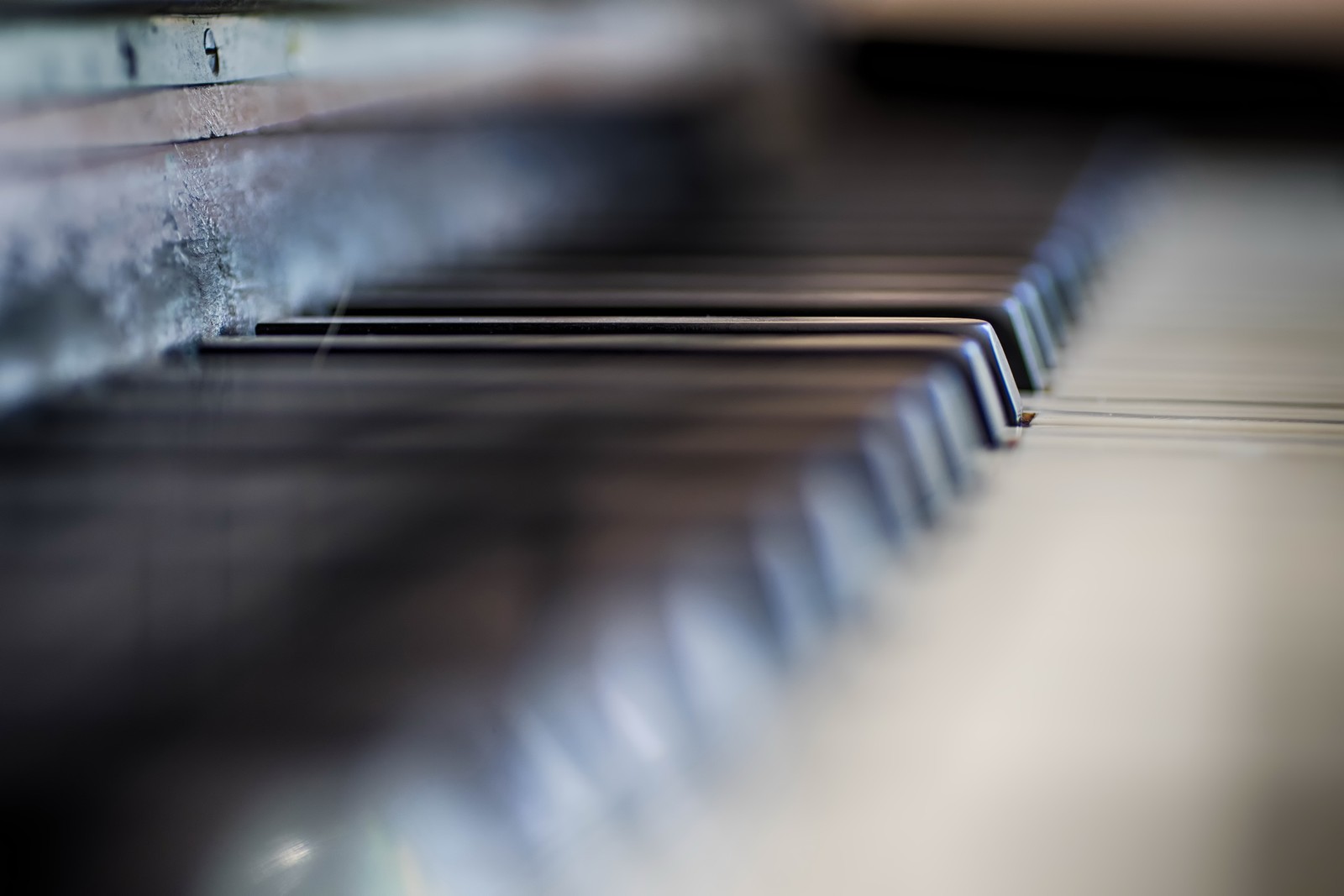 There is a close up of a piano keyboard with a blurry background (piano, line, metal, steel, wood)