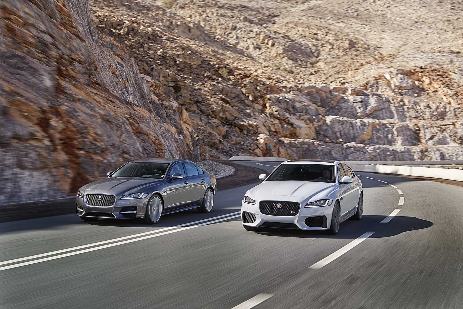 Two silver cars driving down a mountain road next to a mountain (jaguar cars, jaguar, car, sports car, 2016 jaguar xf)