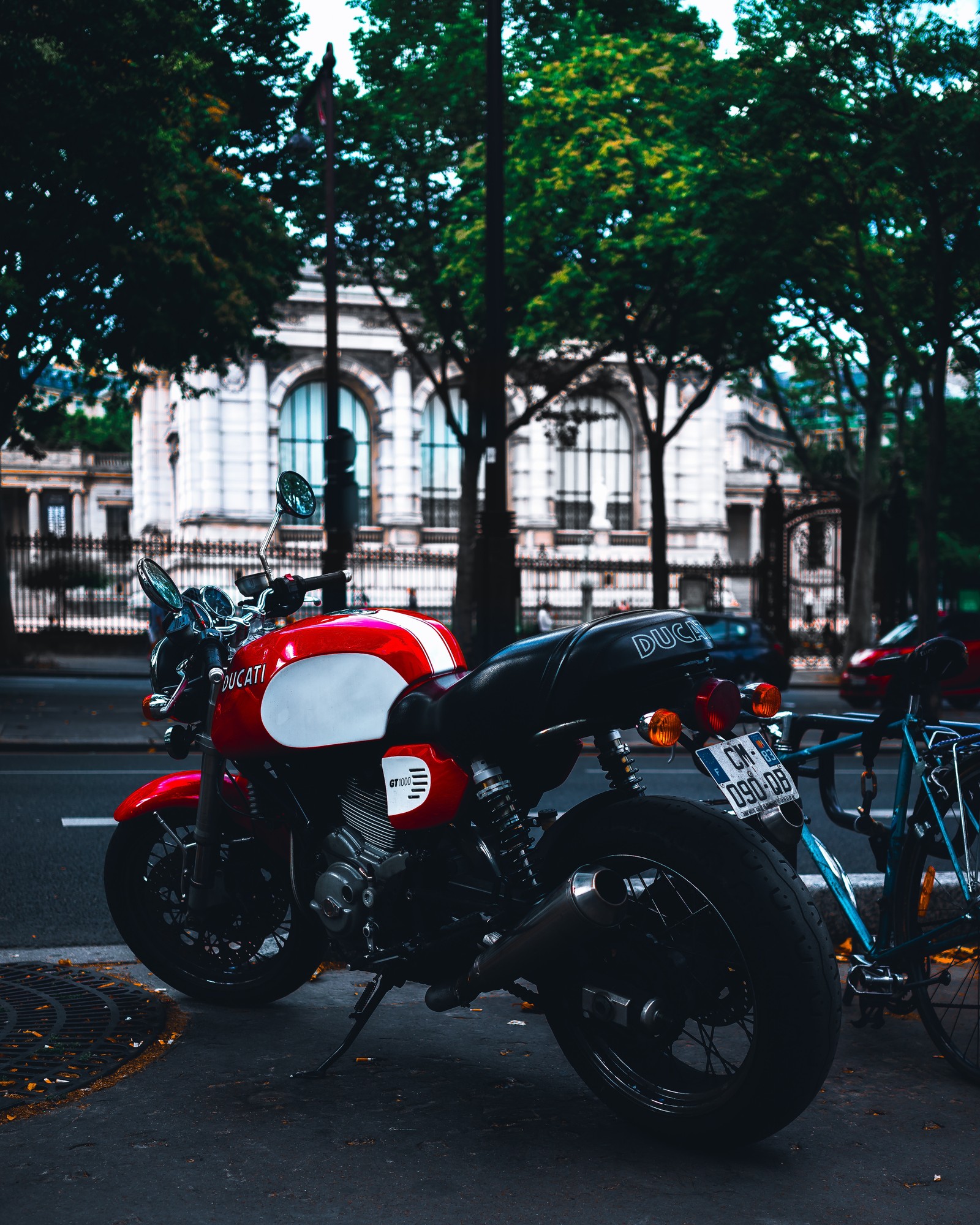 There is a red motorcycle parked on the side of the road (motorcycle, ducati, car, tree, helmet)