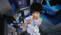 Chaeyoung of TWICE holding white and blue flowers in a retro phone booth, surrounded by a vibrant, neon-lit atmosphere.