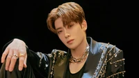 Jaehyun of NCT U exudes charisma and style in a striking black outfit adorned with intricate embellishments, showcasing a captivating gaze against a dark backdrop.