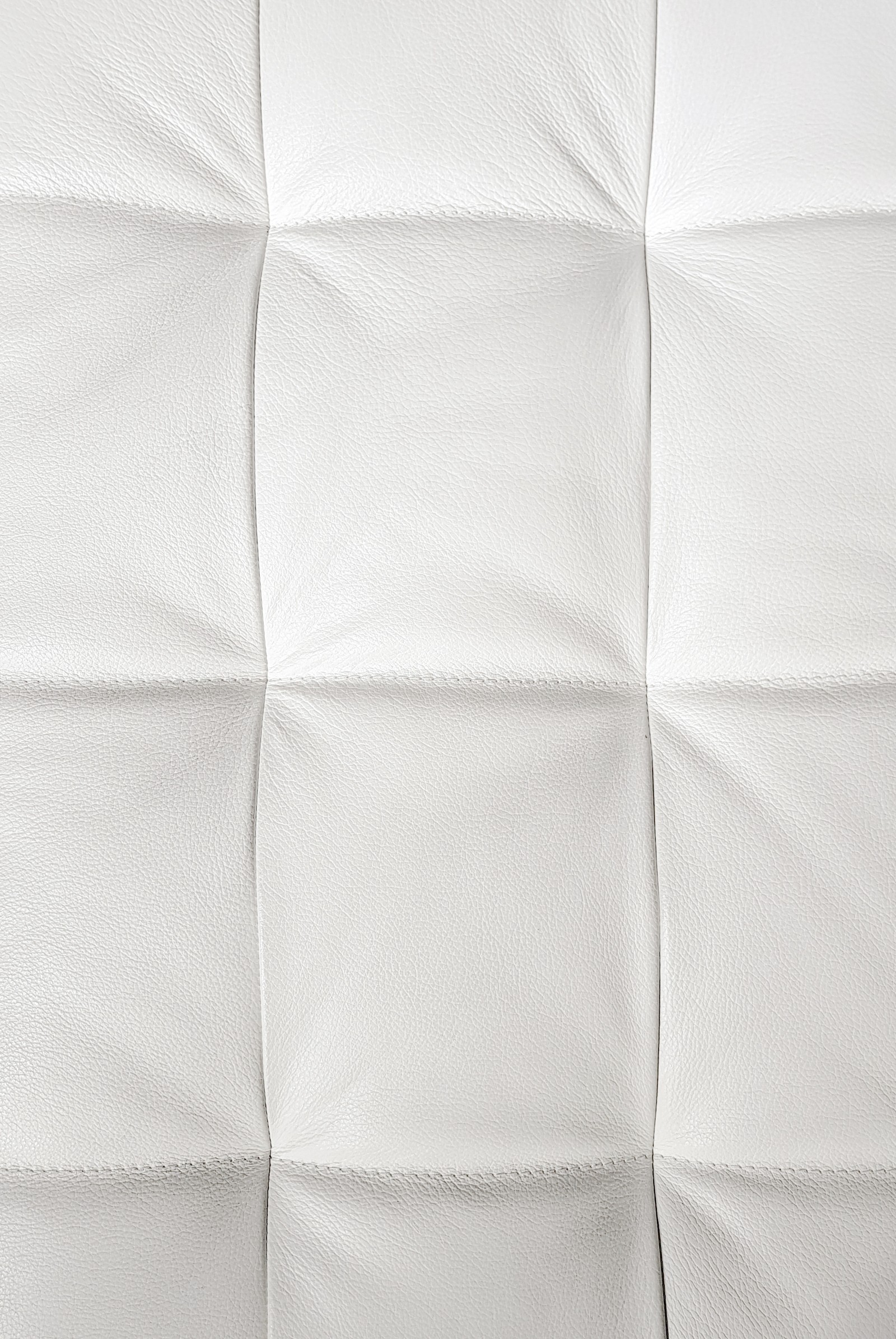 A close up of a white quilted bed with a white pillow (leather, squares, stitches, white, wrinkles)