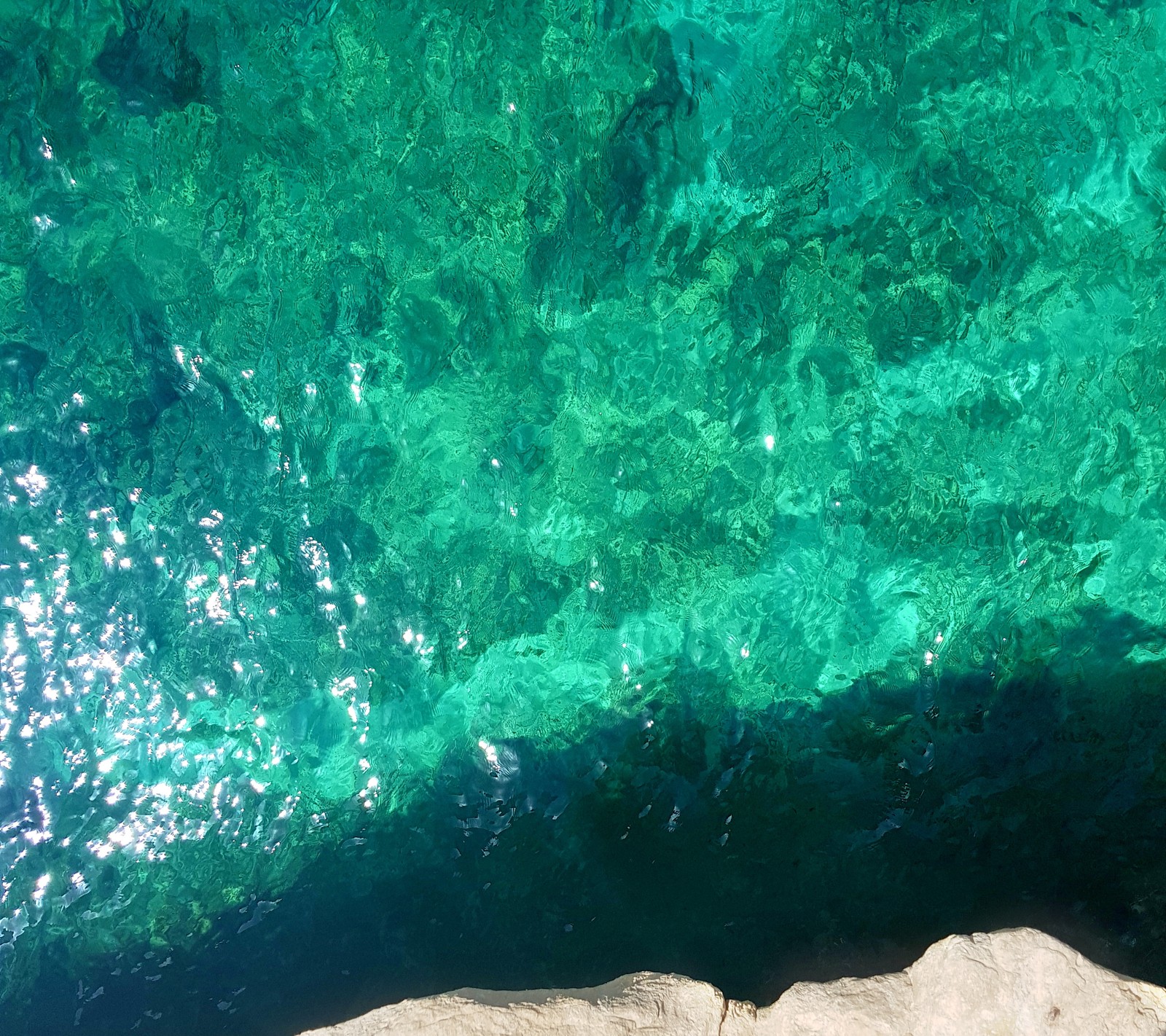 Uma pessoa em pé sobre uma pedra perto da água (praia, bonito, crystal blue, malta, mar)