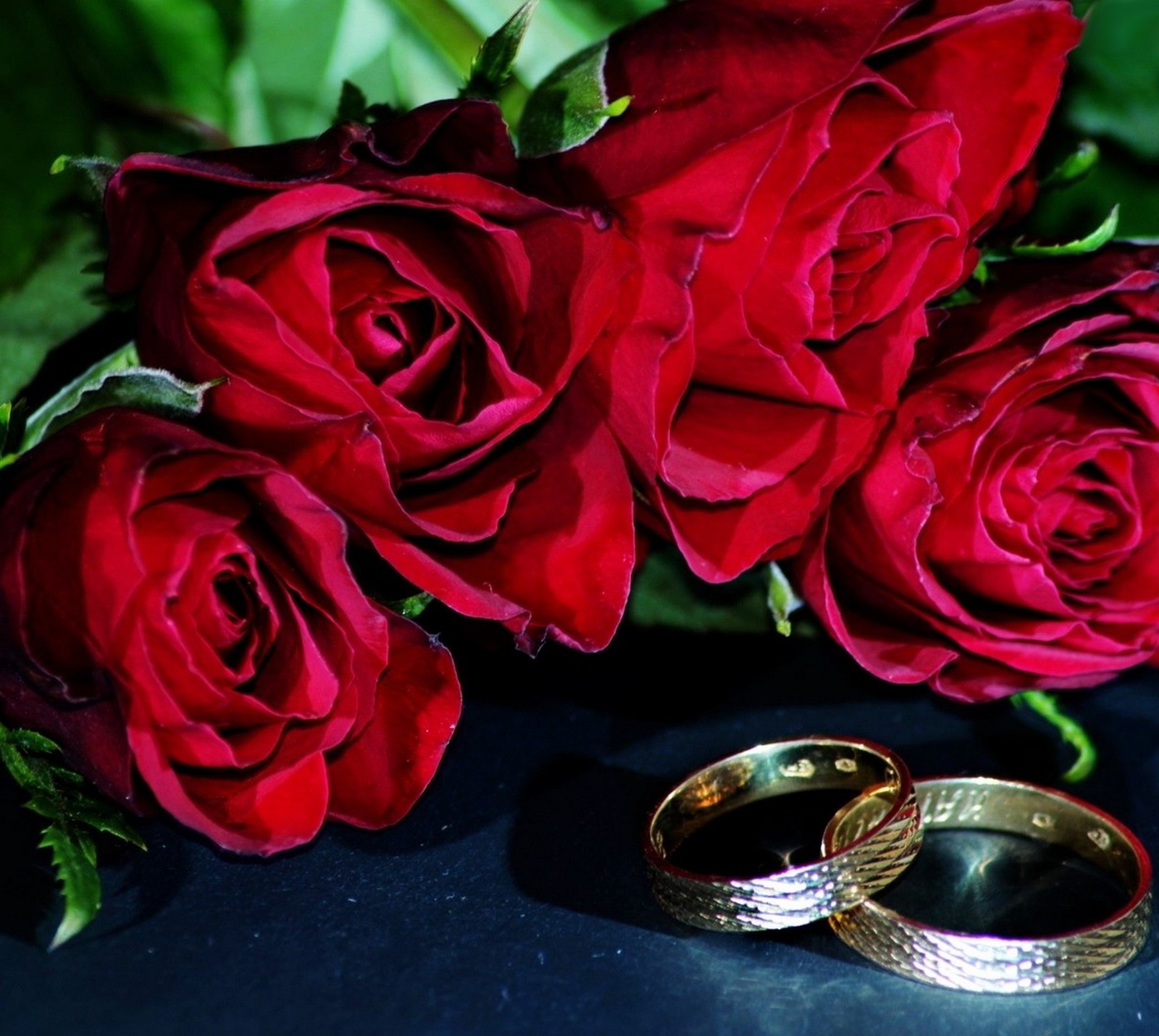 Hay dos anillos de boda y dos rosas sobre una mesa (te quiero, matrimonio, rosas rojas, anillos de boda, you merry me)