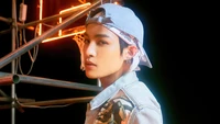 Yangyang von NCT U in einer auffälligen Pose, die eine Mischung aus urbanem Stil und Charisma vor einem lebhaften Neon-Hintergrund zeigt.