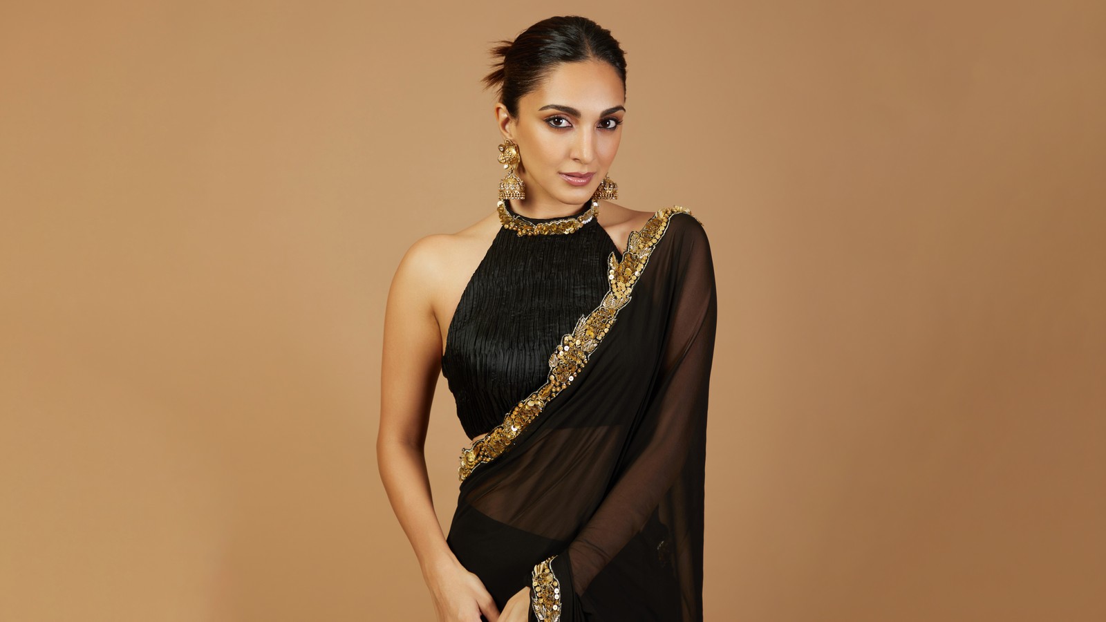 Une femme en sari noir et blouse dorée (kiara advani, sari, saree, beige, arrière plan brun)