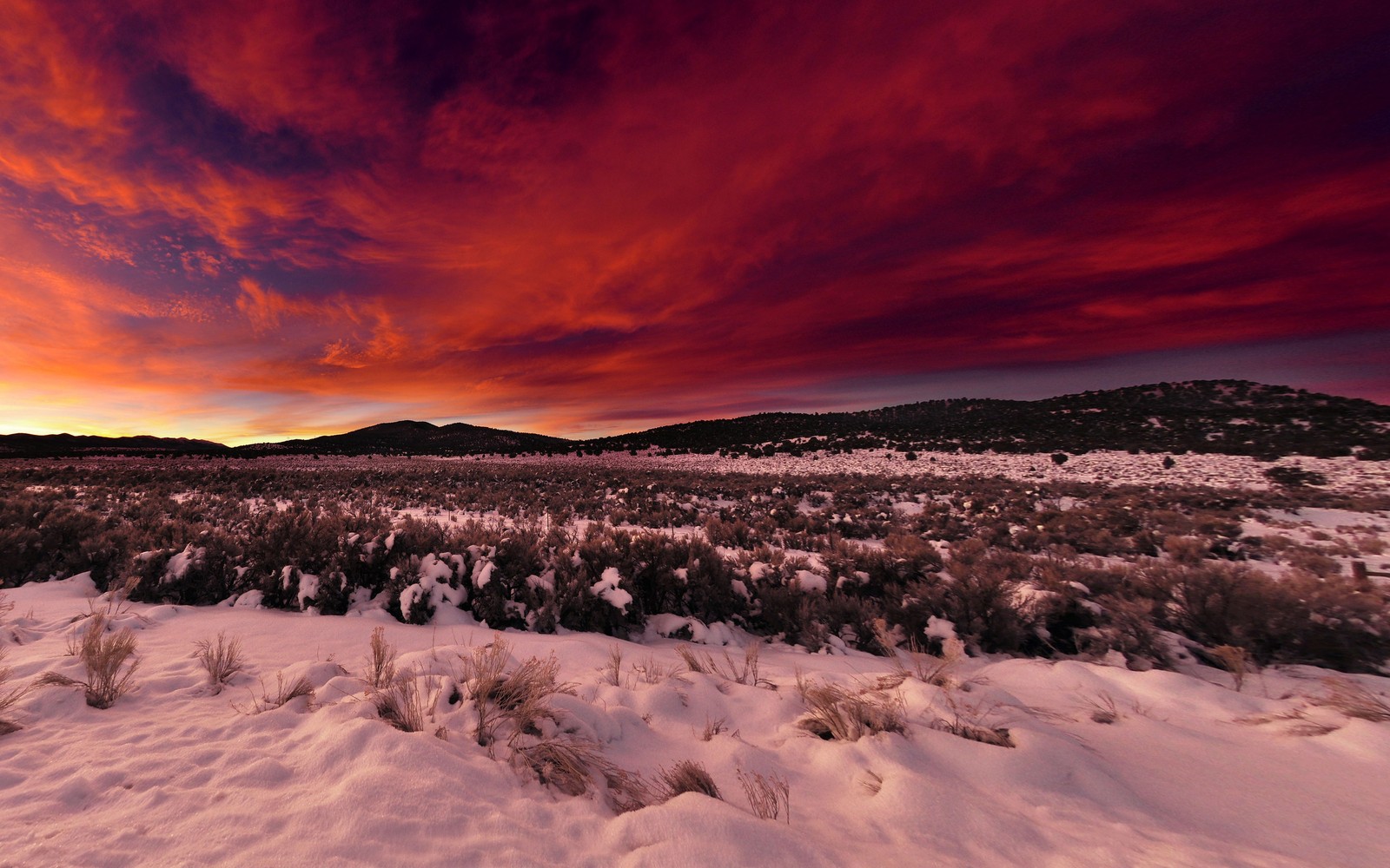 Ciel rouge au-dessus d'un champ enneigé avec une montagne en arrière-plan (hiver, neige, coucher de soleil, nature, nuage)