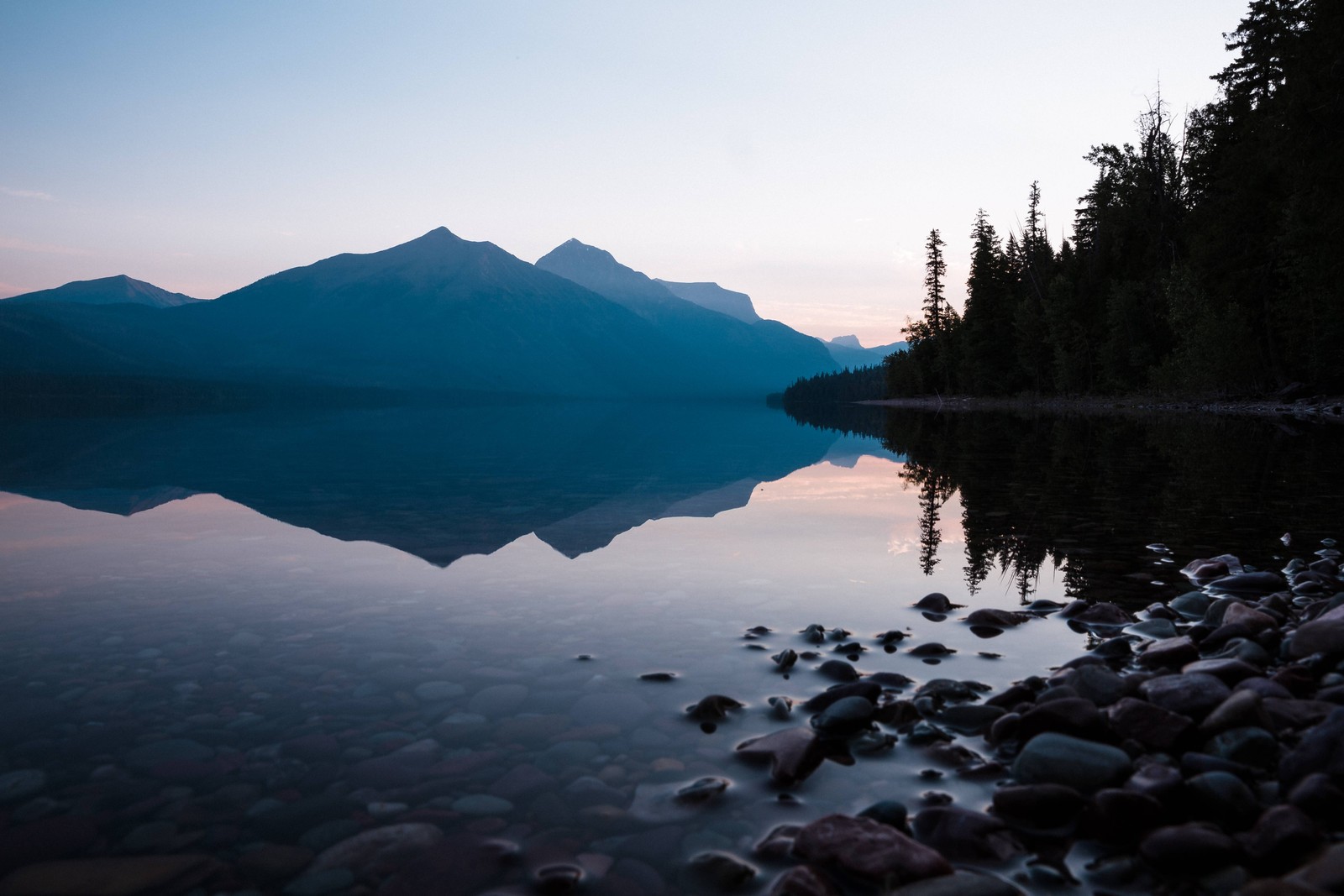 Arafed mountain reflected in a lake at dusk with rocks and trees (reflection, lake, national park, wilderness, nature)