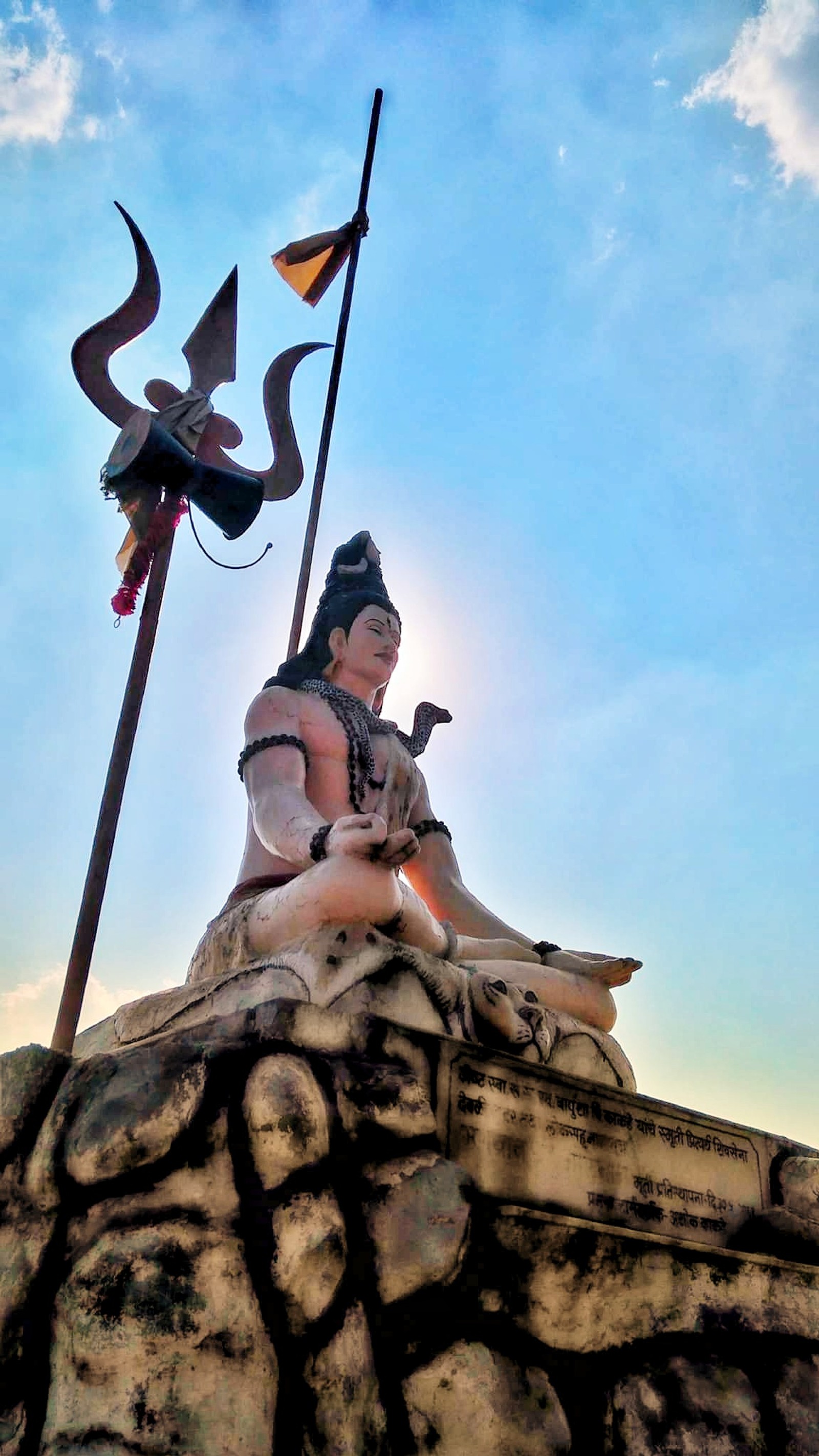 Há uma estátua de um homem sentado em uma rocha com uma bandeira (bholnath, calm wall, deus hindu, senhor shiva, lord shiva)