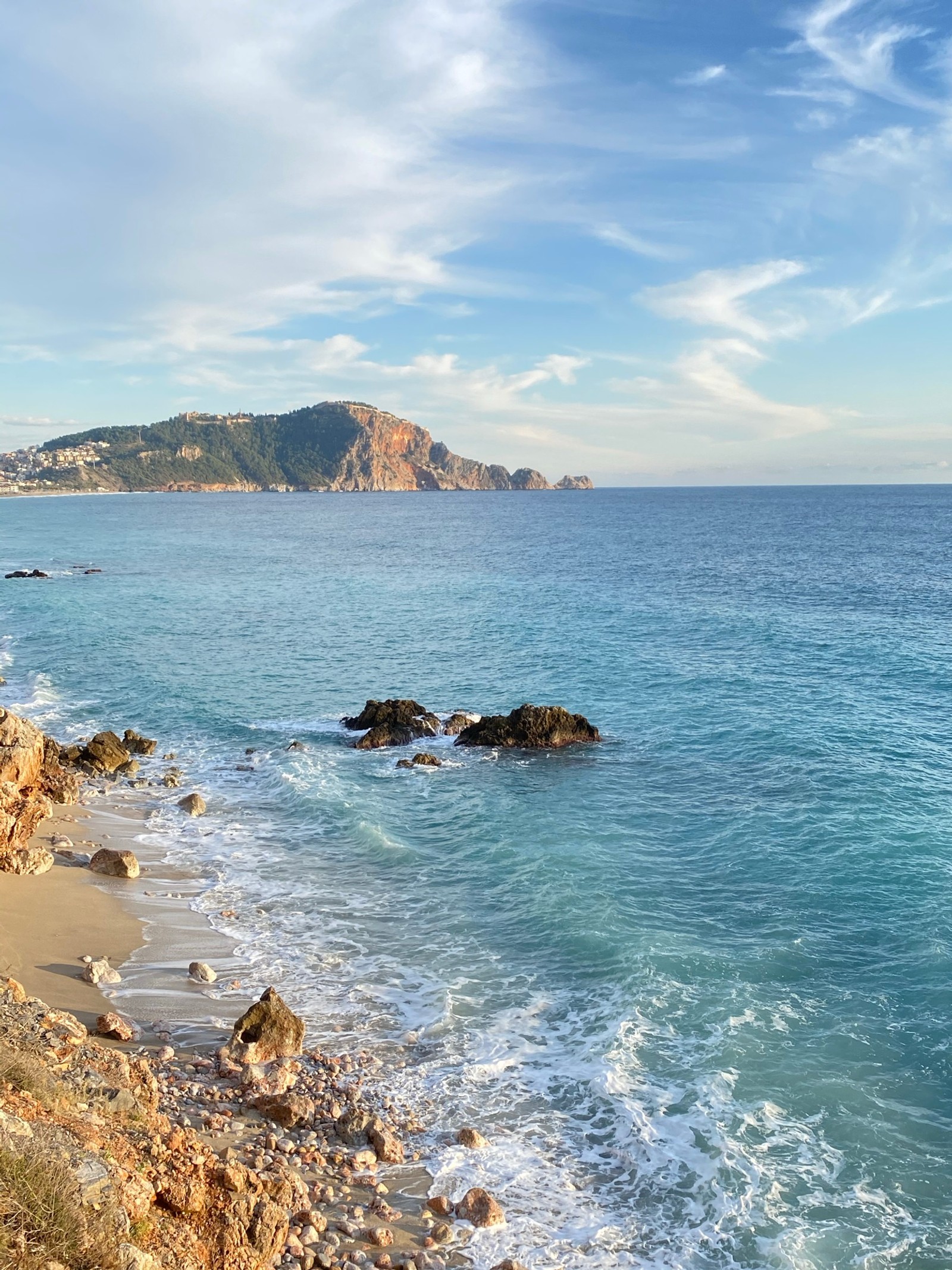 Une vue d'une plage avec un rivage rocheux et une montagne au loin (plage de cléopâtre, la côte, vague de vent, eau, nuage)