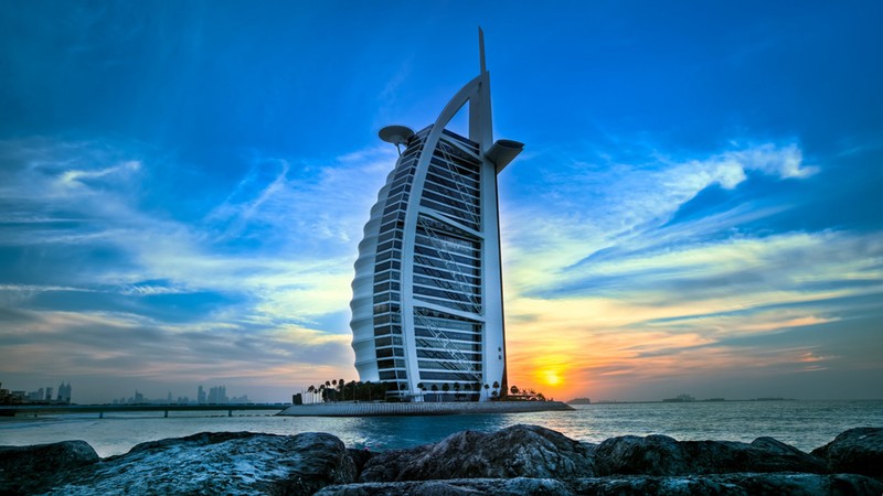 Высокое здание, стоящее на скалистом пляже у океана (бурдж аль араб, burj al arab, мадинат джумейра, madinat jumeirah, пляж джумейра)