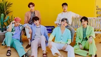 Miembros de Monsta X en trajes coloridos contra un fondo amarillo vibrante