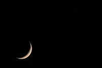 Lune croissante illuminant le ciel nocturne sombre avec un objet céleste lointain