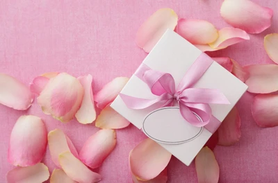 Elegante caja de regalo blanca con cinta rosa rodeada de pétalos de flores