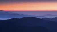 Chaîne de montagnes brumeuse au coucher du soleil avec ciel orange