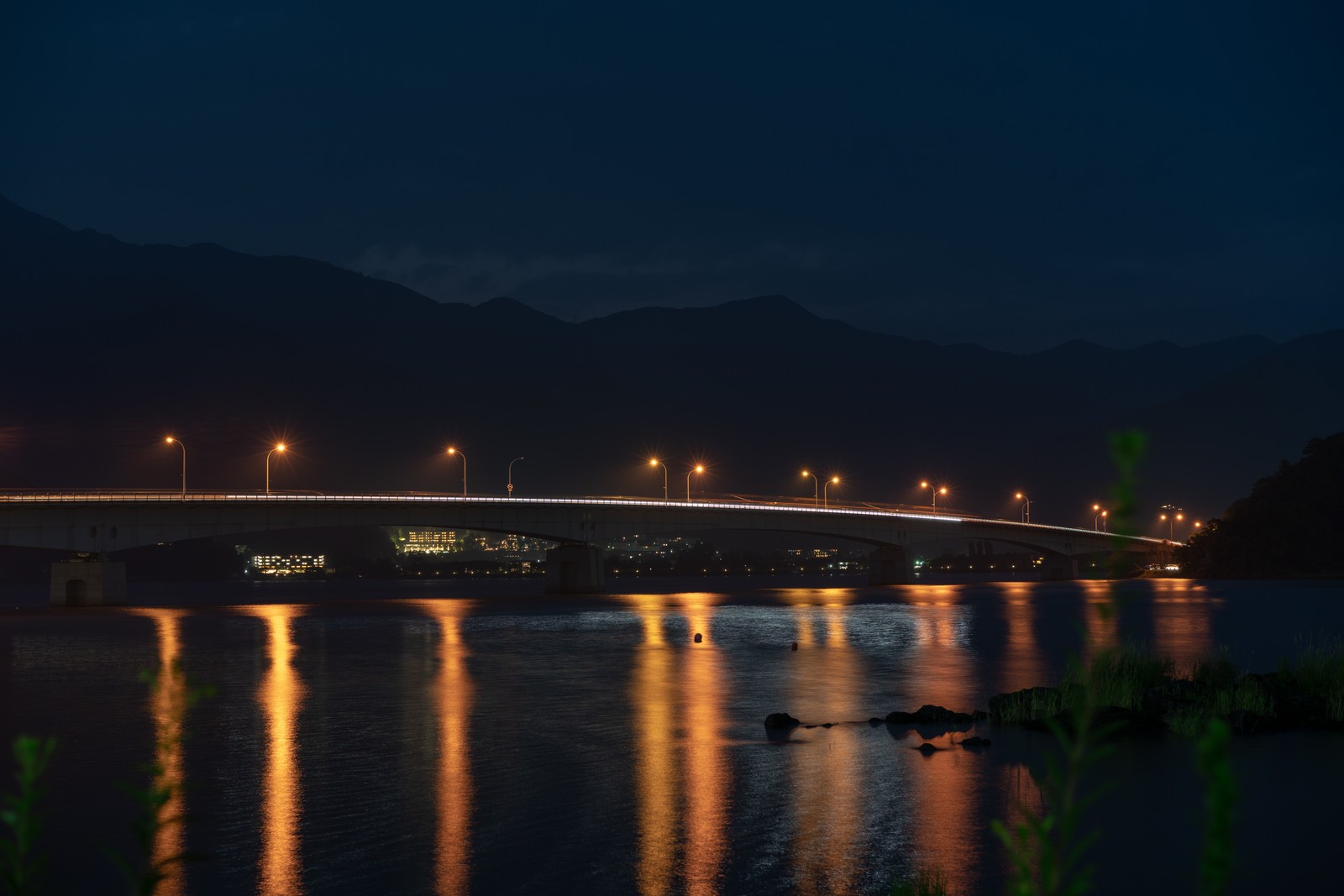 Uma ponte sobre um rio à noite com luzes refletindo na água (iluminação, luz, noite, água, ponte)