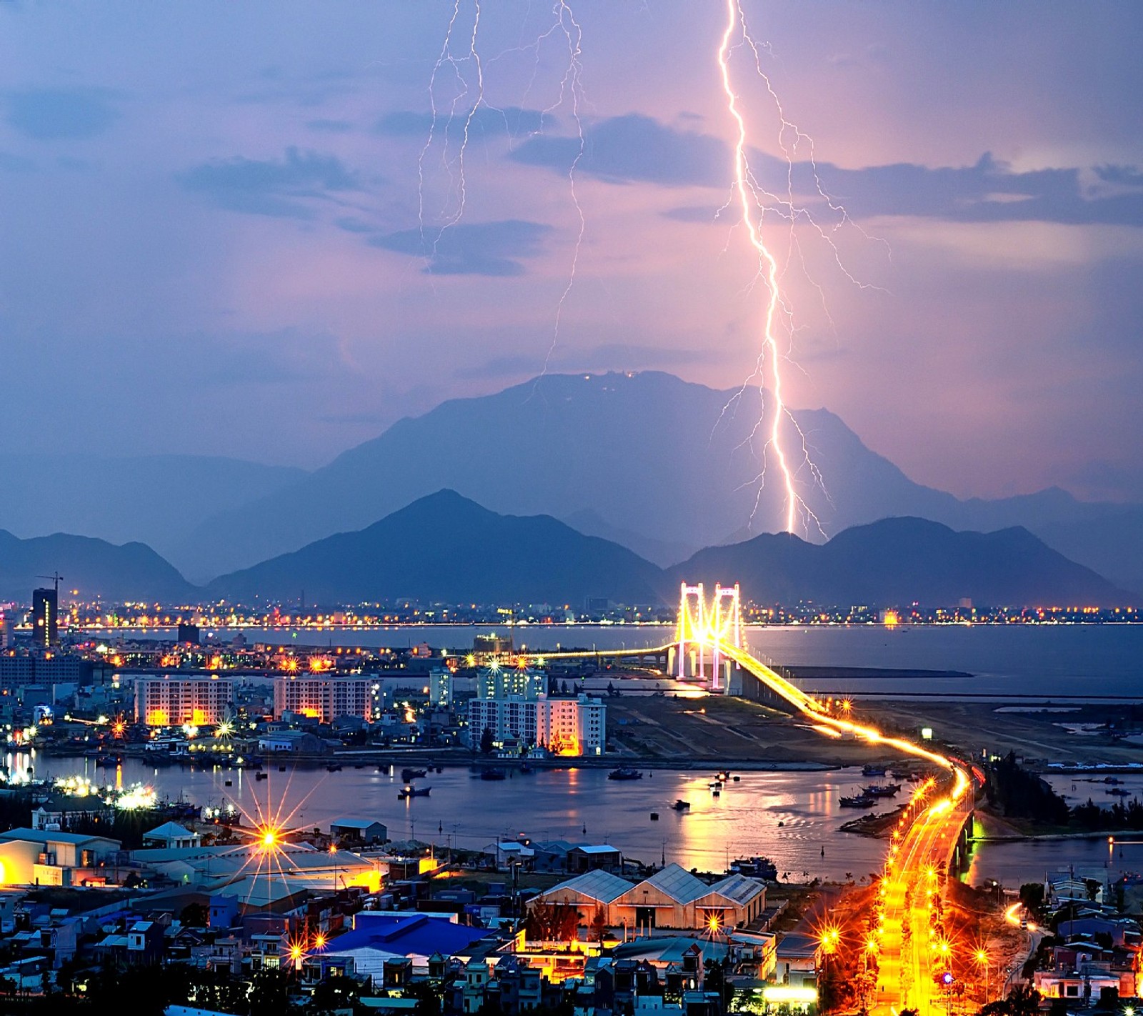 Lightning strikes over a city and a bridge in the distance (nature)