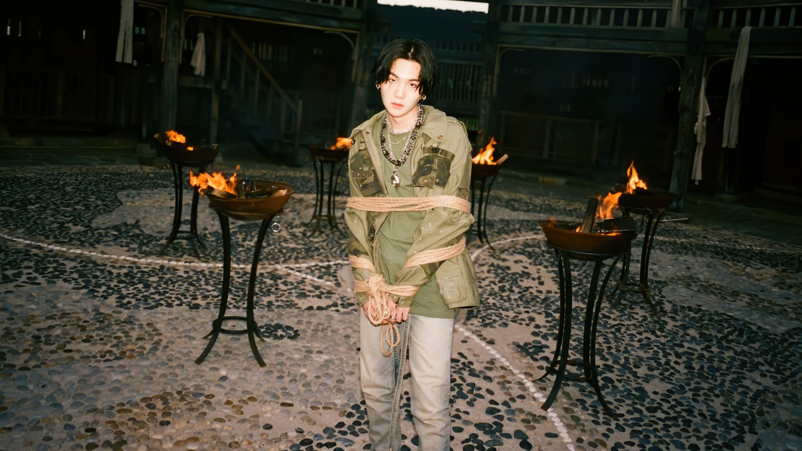 There is a woman standing in front of a fire pit (agust d, daechwita, 대취타, suga, 슈가)