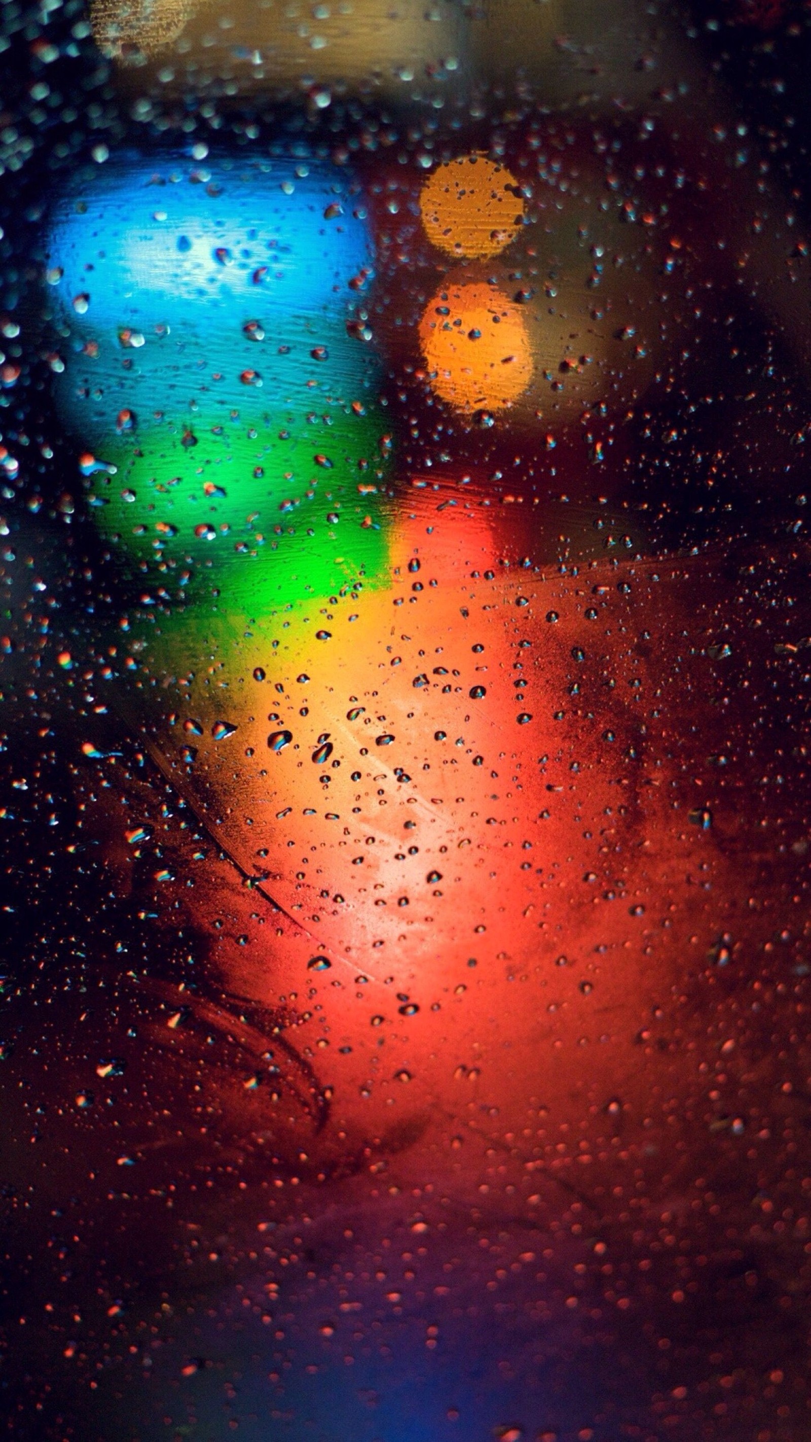 Um close de uma janela coberta de chuva com uma luz colorida ao fundo (água, retrato, gráficos, gota, laranja)