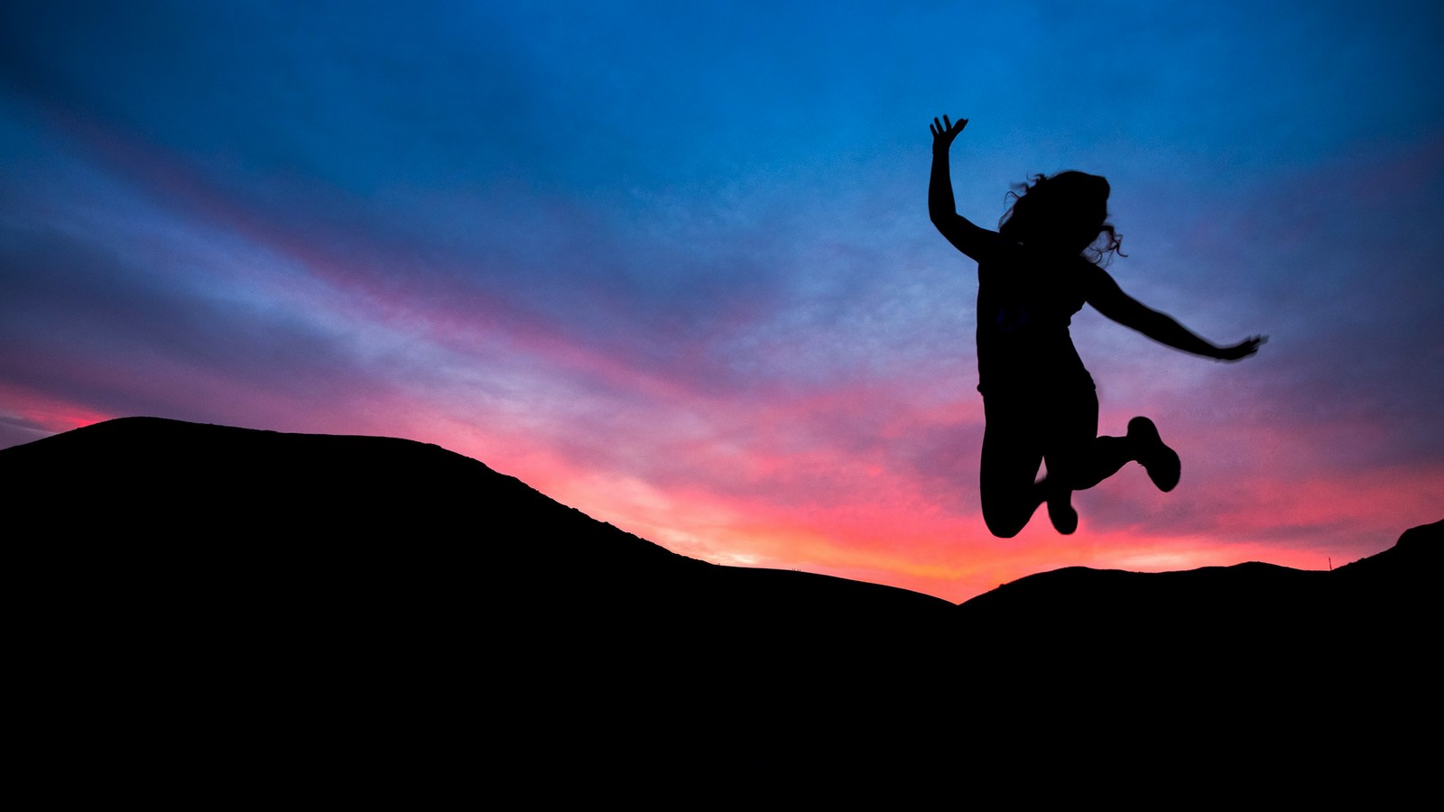 Une femme sautant en l'air au coucher du soleil les bras écartés (personne, silhouette, coucher de soleil, sauter, humeur)